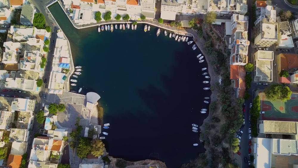 A stunning aerial view of Lake Voulismeni in Agios Nikolaos, Crete, showcasing the serene blue water surrounded by boats and buildings. | Cheap Car Rental